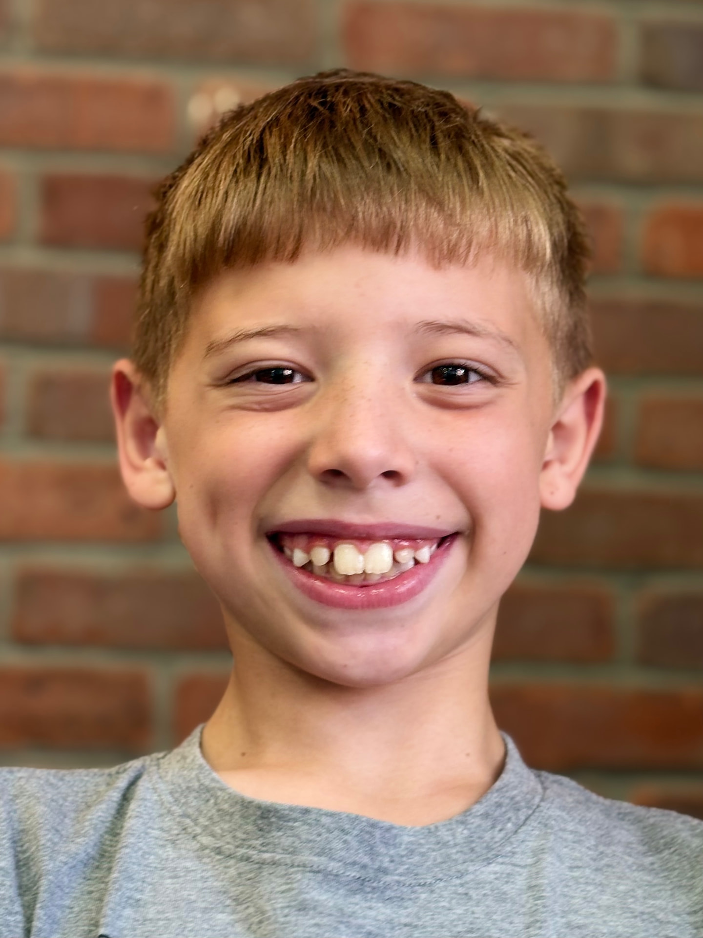 Young orthodontic patient smiling by the office brick wall